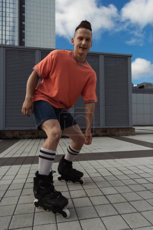 Smiling roller skater in casual clothes looking at camera on urban street 