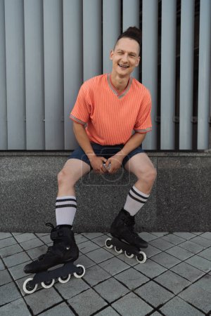 Photo for Cheerful man in casual clothes and roller skates looking at camera on urban street - Royalty Free Image