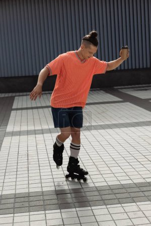 Man in casual clothes holding coffee to go and roller skating outdoors 