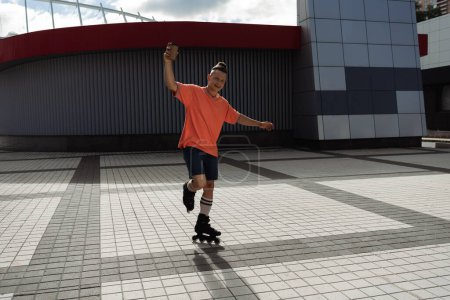 Téléchargez les photos : Joyeux patineur à roulettes tenant à emporter boisson et équitation sur la rue urbaine - en image libre de droit