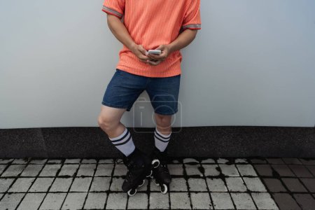 Cropped view of man in roller skates using cellphone near wall outdoors 