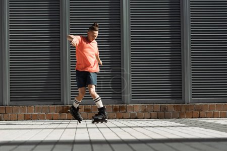 Foto de Joven patinador en pantalones cortos y calcetines de rodilla haciendo truco en la calle urbana - Imagen libre de derechos