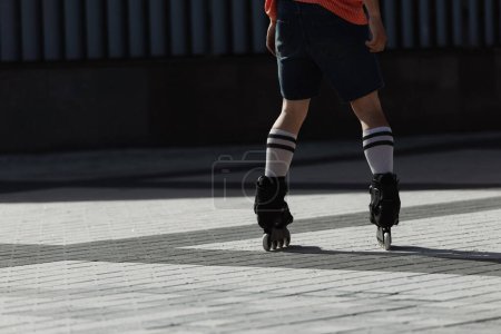 Cropped view of young man in shorts and roller skates riding on city square at daytime 