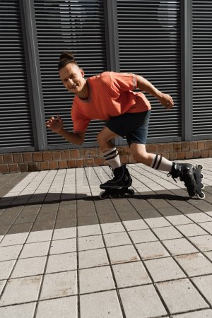Hombre positivo mirando a la cámara mientras patina en la calle urbana 