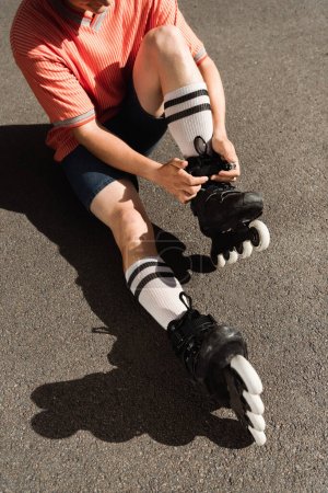 Vista recortada del hombre en pantalones cortos con patines sobre asfalto 