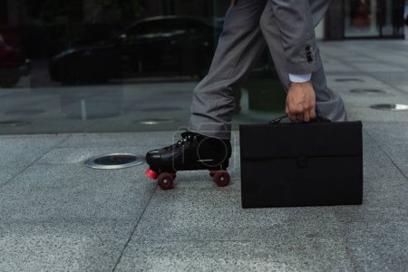 cropped view of roller skater in formal wear holding black briefcase on street