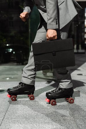 partial view of businessman with black briefcase rollerskating on city street