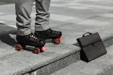 Téléchargez les photos : Vue partielle de l'homme d'affaires en patins à roulettes debout près de la mallette noire sur la rue de la ville - en image libre de droit