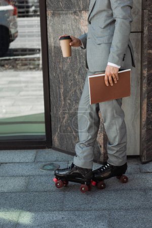 Photo for Cropped view of businessman in roller skates standing with folder and takeaway drink near building on street - Royalty Free Image