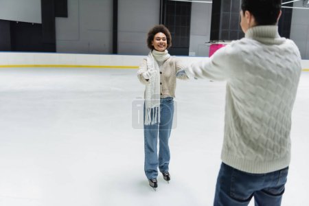Photo for Cheerful african american woman outstretching hands to blurred boyfriend on ice rink - Royalty Free Image