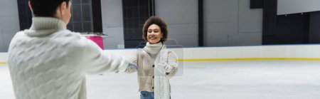 Photo for Young african american woman outstretching hands to boyfriend on ice rink, banner - Royalty Free Image