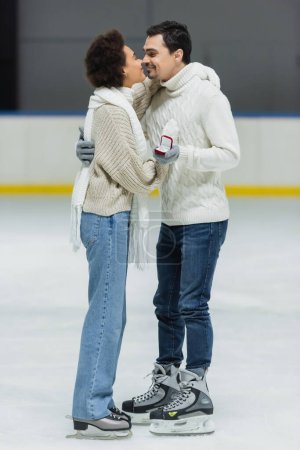 Foto de Vista lateral de pareja multiétnica con anillo de propuesta besándose en pista de hielo - Imagen libre de derechos