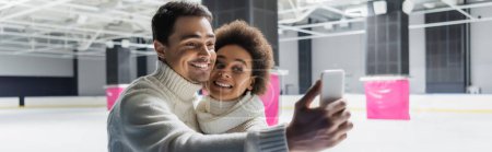 Photo for Cheerful man taking selfie with african american girlfriend on ice rink, banner - Royalty Free Image