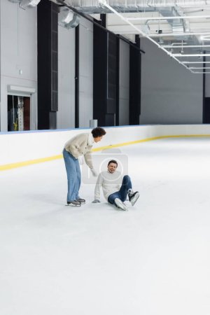 African american woman helping boyfriend sitting on ice rink 