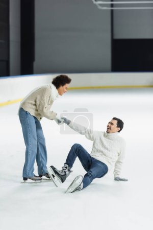 Cheerful african american woman holding hand of boyfriend on ice rink 