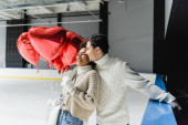 Pleased man in sweater hugging african american girlfriend with heart shaped balloons on ice rink  puzzle #625351448