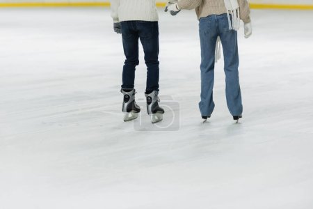 Cropped view of couple holding hands and ice skating on rink 