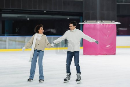 Photo pour Femme afro-américaine excitée patinage sur glace avec petit ami sur la patinoire - image libre de droit