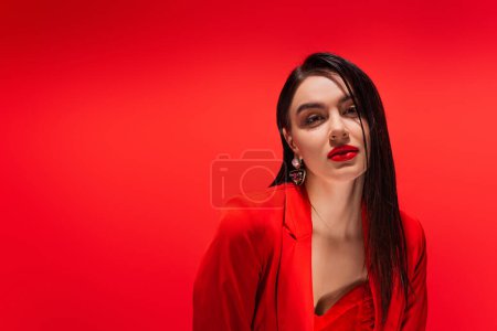 Portrait of elegant woman in jacket looking at camera isolated on red 