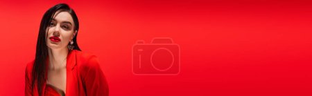 Photo for Portrait of young brunette woman in jacket looking at camera isolated on red, banner - Royalty Free Image
