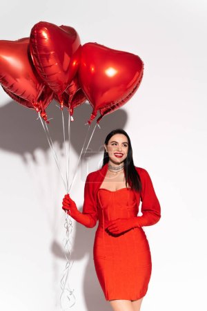 Photo for Cheerful brunette woman holding red heart shaped balloons on white background - Royalty Free Image