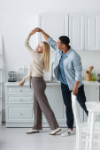 full length of happy interracial couple holding hands while dancing in kitchen Poster #625475120
