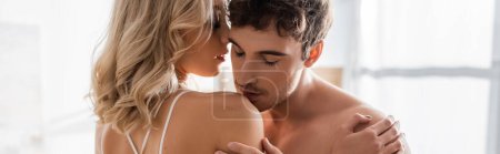 Young man kissing shoulder of blonde girlfriend at home, banner 
