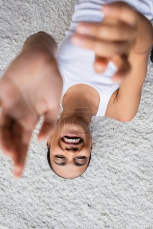 top view of positive african american woman in tank top lying on carpet 