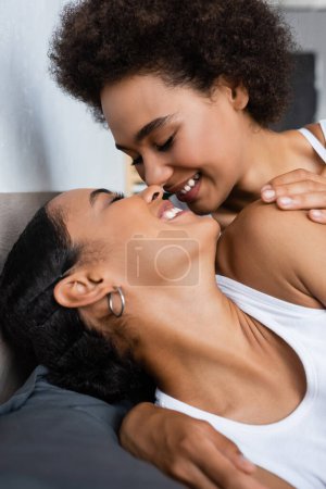 freudige und lesbische afrikanisch-amerikanische Frau mit geschlossenen Augen küsst Freundin auf dem Bett