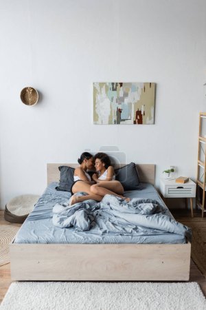 Téléchargez les photos : Sourire lesbienne afro-américain couple étreignant l'autre tout en étant couché dans la chambre moderne - en image libre de droit