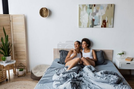 Photo for Cheerful lesbian african american woman hugging girlfriend in modern bedroom - Royalty Free Image