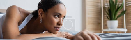 young african american woman lying on bed and looking away, banner
