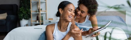 Téléchargez les photos : Heureux afro-américaine femme pointant avec la main à portable près de petite amie, bannière - en image libre de droit