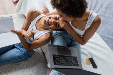 top view of happy african american woman with laptop laughing near girlfriend  