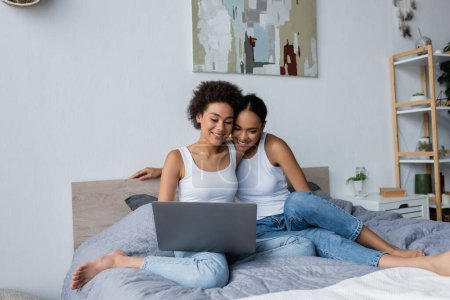 african american lesbian couple looking at laptop while watching movie in bedroom
