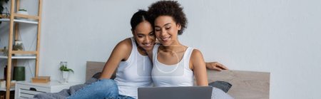 african american lesbian couple looking at laptop while watching movie in bedroom, banner
