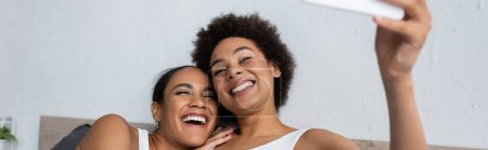 happy african american lesbian couple taking selfie on smartphone at home, banner