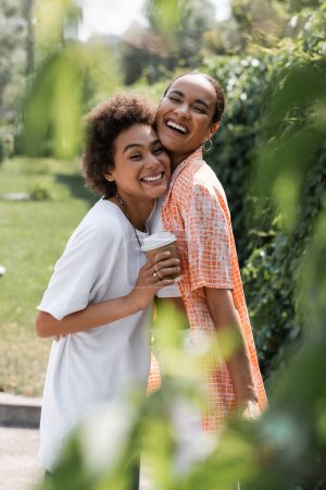 happy african american lesbian couple holding coffee to go in park 