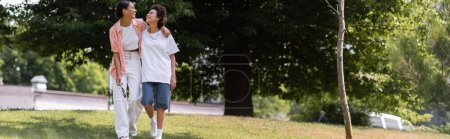 volle Länge der jungen afrikanisch-amerikanischen Frau umarmt lesbischen Partner und zu Fuß in grünen Park, Banner