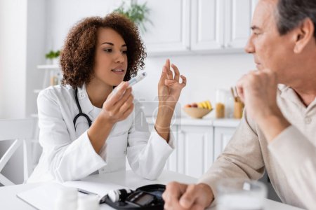 Photo for Curly african american doctor explaining how to use lancet pen to middle aged patient with diabetes - Royalty Free Image