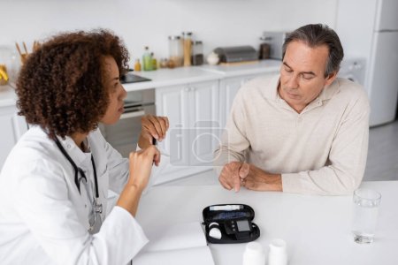 middle aged man with diabetes pointing at lancet pen device while talking with curly african american doctor