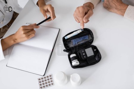 Draufsicht von Mann mittleren Alters mit Diabetes zeigt auf Lanzet Pen Gerät in der Nähe afrikanisch-amerikanischer Arzt