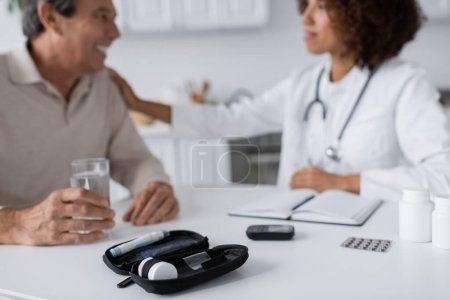 glucose meter and lancet pen devices near african american doctor and middle aged man with diabetes on blurred background 