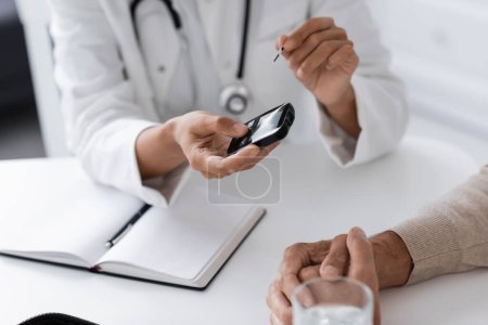 cropped view of african american doctor holding glucometer device near middle aged patient
