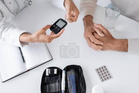 Photo for Top view of african american doctor showing glucometer device and test strip to middle aged patient - Royalty Free Image