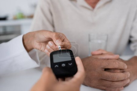 Téléchargez les photos : Vue partielle du médecin afro-américain montrant la bande de test sur le dispositif de glucomètre au patient d'âge moyen - en image libre de droit