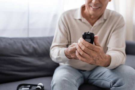 Téléchargez les photos : Vue partielle de l'homme d'âge moyen joyeux avec diabète tenant appareil de mesure de glucose - en image libre de droit