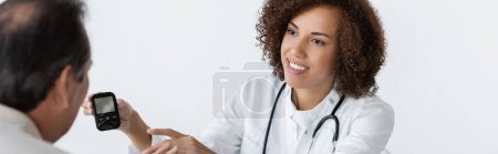 joyeux médecin afro-américain pointant du doigt le glucomètre près d'un homme d'âge moyen diabétique à la clinique, bannière
