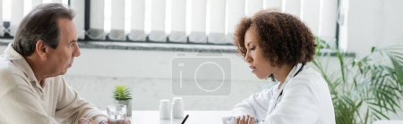 african american doctor writing prescription near mature patient with diabetes holding glass of water in clinic, banner