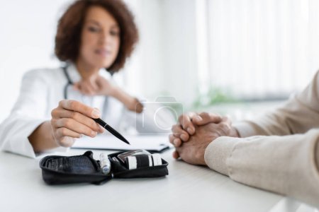 Photo for Blurred african american doctor pointing at diabetes kit near patient in clinic - Royalty Free Image